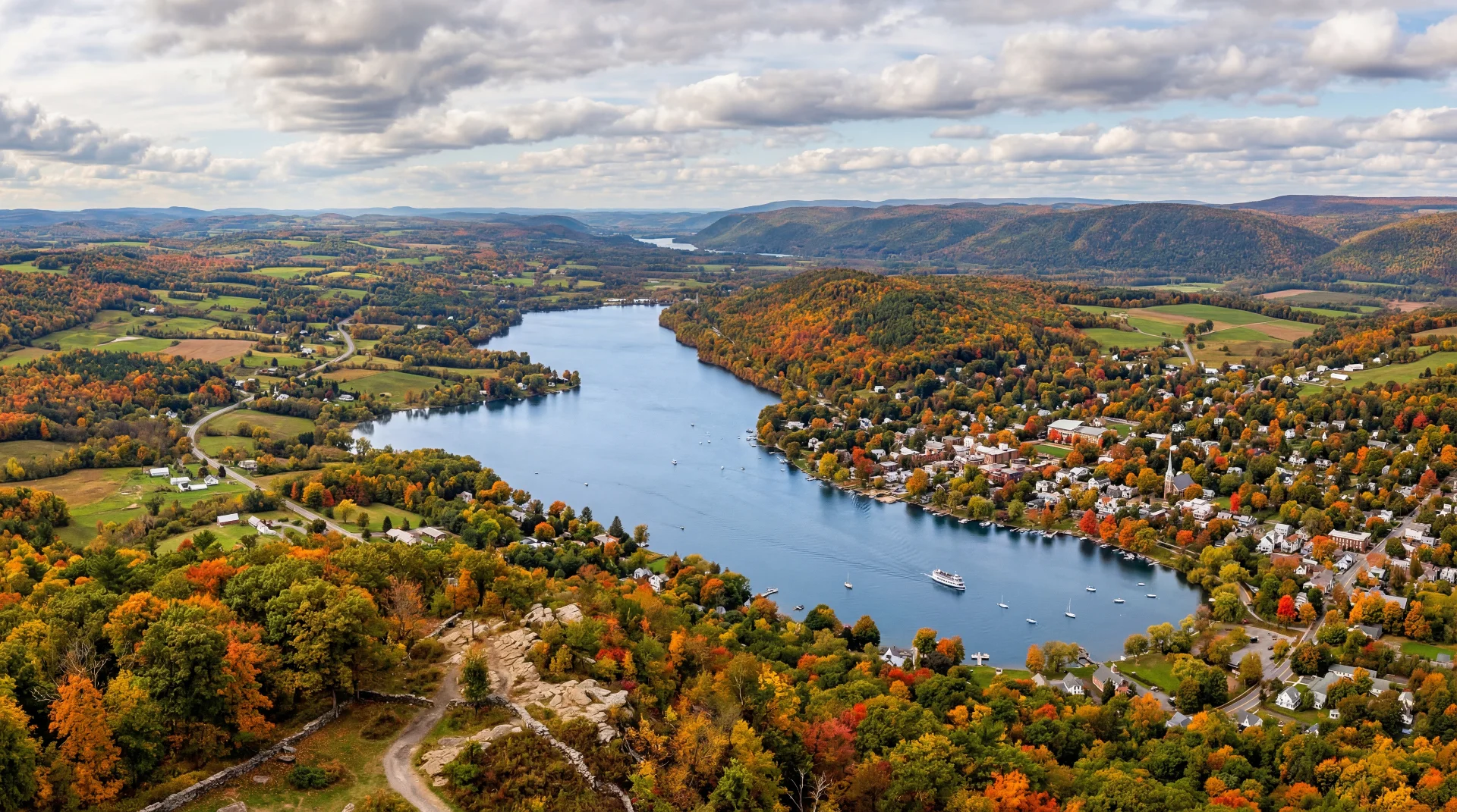 Panoramic view of the Otsego County countryside featuring rolling green hills, farmland, and a distant village in autumn light.