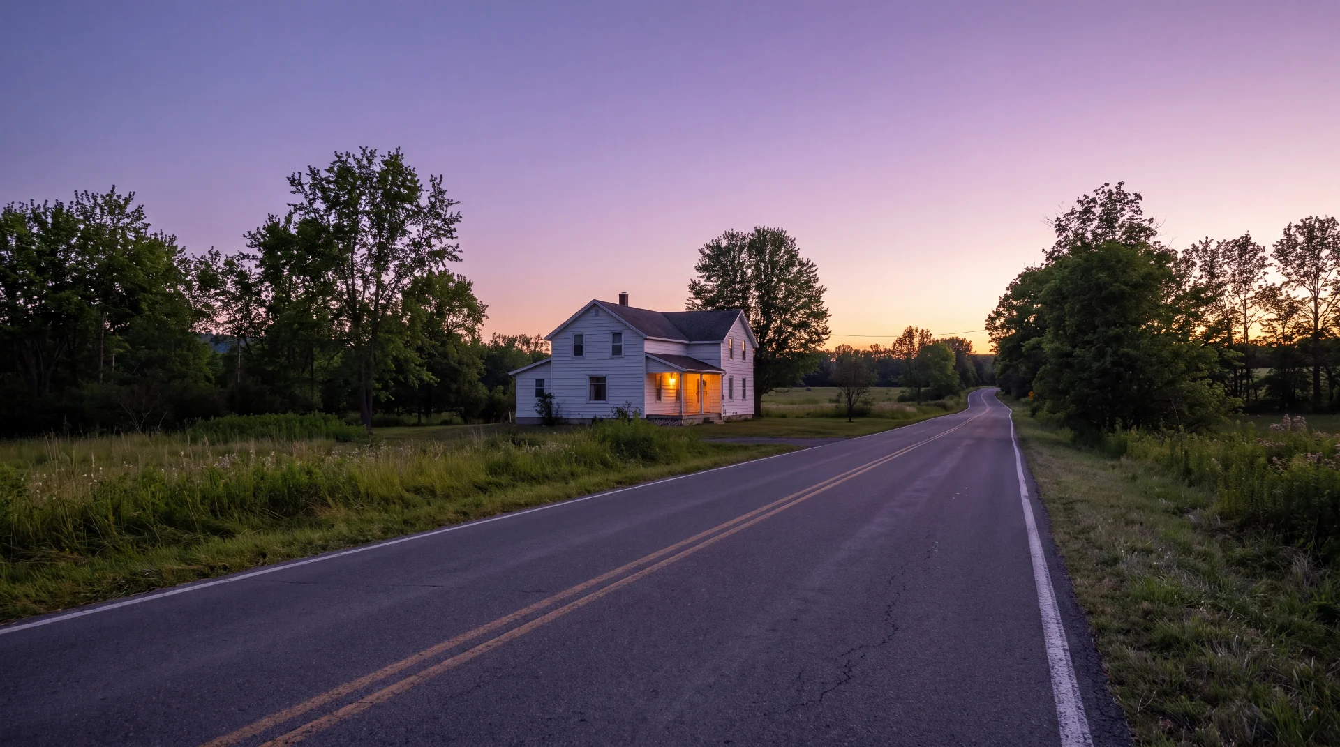 Farmhouse porch light at dusk along a quiet Upstate New York country road